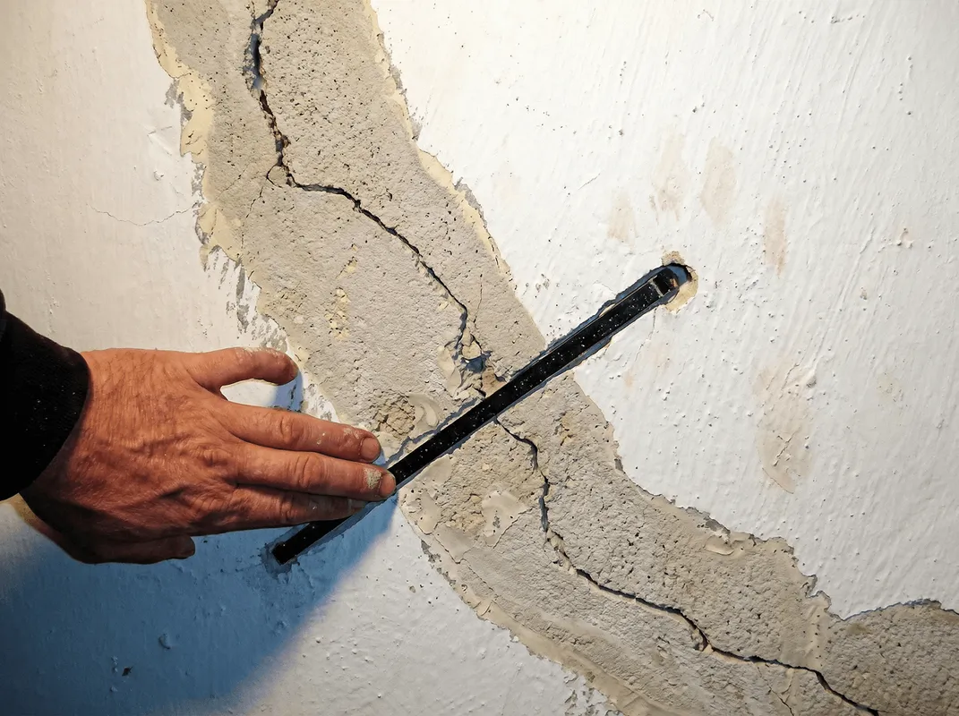 A wall with a large crack is being inspected by a professional in Overland Park, KS